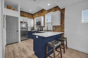 Kitchen featuring a breakfast bar, a peninsula, white cabinets, stainless steel appliances, and light wood finished floors