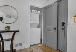 Clothes washing area with light wood-style flooring, visible vents, laundry area, and stacked washer / drying machine