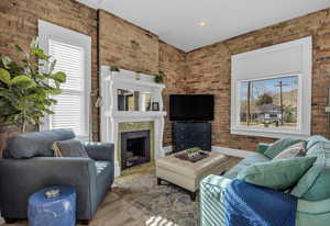 Living room featuring brick wall, a fireplace, and wood finished floors