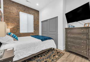Bedroom featuring brick wall, visible vents, a closet, and wood finished floors