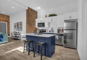 Kitchen with white cabinets, a sink, appliances with stainless steel finishes, light wood finished floors, and a kitchen island