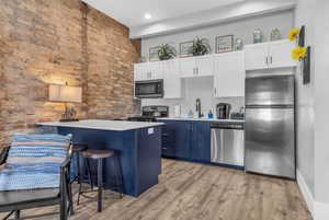 Kitchen featuring blue cabinets, a sink, stainless steel appliances, light wood finished floors, and a breakfast bar area
