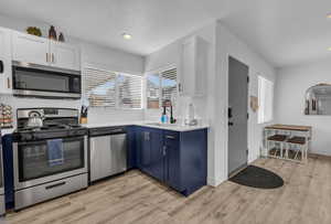 Kitchen with a wealth of natural light, a sink, blue cabinetry, and appliances with stainless steel finishes