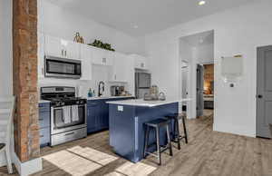 Kitchen with a breakfast bar, appliances with stainless steel finishes, blue cabinets, a sink, and light wood finished floors
