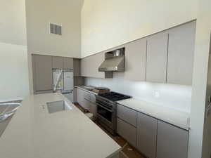 Kitchen with gray cabinets, high end stainless steel range, freestanding refrigerator, a high ceiling, and light countertops