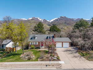 Cape cod house with fence, a front lawn, an attached garage, a mountain view, and driveway