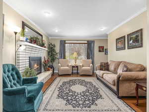 Living room featuring wood finished floors, baseboards, ornamental molding, and a brick fireplace