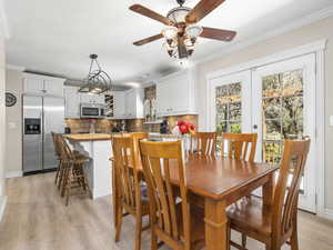 Dining area featuring light wood finished floors, baseboards, a ceiling fan, and crown molding