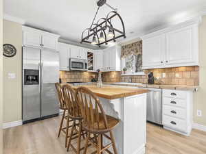 Kitchen featuring butcher block countertops, a kitchen island, white cabinets, light wood-style floors, and appliances with stainless steel finishes