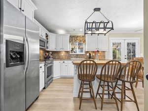Kitchen with white cabinets, a healthy amount of sunlight, appliances with stainless steel finishes, and a textured ceiling