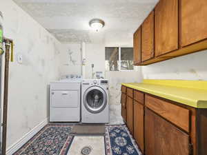 Laundry area featuring a textured ceiling, washing machine and clothes dryer, baseboards, and cabinet space