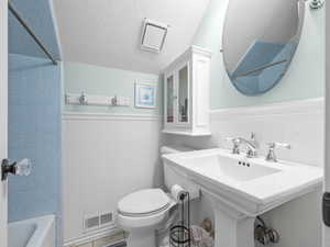 Bathroom featuring toilet, visible vents, a wainscoted wall, and tub / shower combination