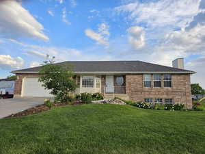 Single story home featuring concrete driveway, a chimney, brick siding, an attached garage, and a front yard