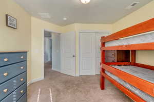 Bedroom with a closet, light colored carpet, baseboards, and visible vents