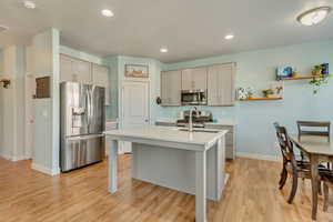 Kitchen with baseboards, light countertops, light wood-type flooring, a kitchen island with sink, and stainless steel appliances