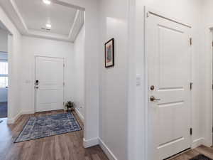 Foyer entrance featuring a raised ceiling, baseboards, and wood finished floors