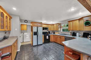 Kitchen featuring glass insert cabinets, washer and dryer, a sink, recessed lighting, and stainless steel appliances