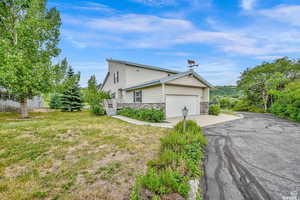 View of side of property featuring a lawn, an attached garage, stone siding, and driveway