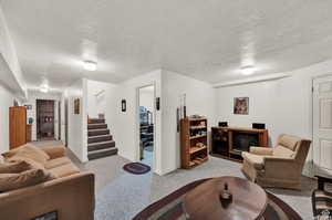 Living area featuring carpet floors, baseboards, stairs, and a textured ceiling