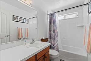 Full bathroom with toilet, a textured ceiling, vanity, and shower / tub combo with curtain
