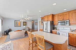 Kitchen featuring a kitchen breakfast bar, light wood-style flooring, brown cabinetry, light countertops, and stainless steel appliances