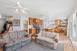 Living room with visible vents, light wood-type flooring, a ceiling fan, and a healthy amount of sunlight