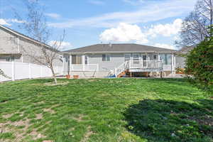 Rear view of property with fence, a yard, a deck, and a sunroom