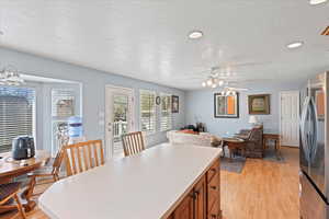 Kitchen featuring light wood-style flooring, a textured ceiling, freestanding refrigerator, a ceiling fan, and brown cabinets