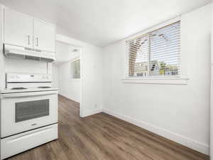 Kitchen featuring dark wood finished floors, a textured ceiling, under cabinet range hood, white range with electric stovetop, and baseboards