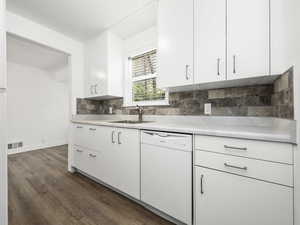 Kitchen with dark wood-type flooring, white cabinetry, dishwasher, light countertops, and a sink