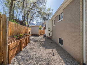 View of property exterior with an outbuilding, a storage shed, cooling unit, a fenced backyard, and brick siding