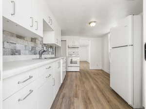 Kitchen featuring white appliances, wood finished floors, under cabinet range hood, light countertops, and decorative backsplash