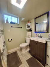Full bathroom with toilet, vanity, wood finished floors, and baseboards