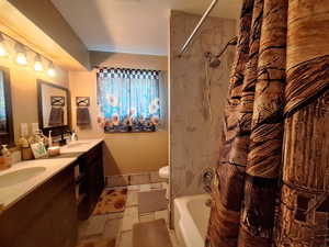 Full bathroom with toilet, stone tile floors, double vanity, and a sink