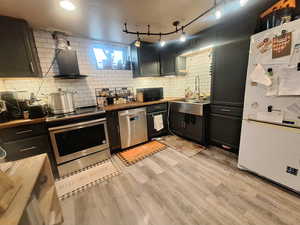 Kitchen with light wood-style floors, dark cabinets, tasteful backsplash, stainless steel appliances, and wooden counters