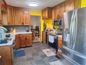 Kitchen with brown cabinets, backsplash, light countertops, and appliances with stainless steel finishes