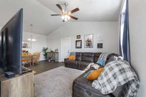Carpeted living area featuring ceiling fan with notable chandelier, baseboards, and lofted ceiling