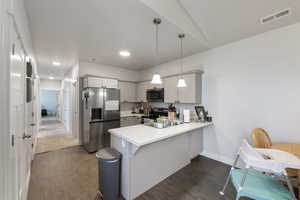Kitchen with visible vents, light countertops, appliances with stainless steel finishes, a peninsula, and dark wood finished floors