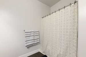 Bathroom with curtained shower, wood finished floors, and baseboards