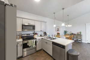 Kitchen with dark wood-type flooring, a peninsula, light countertops, a sink, and stainless steel appliances