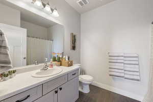 Bathroom with visible vents, baseboards, toilet, vanity, and wood finished floors