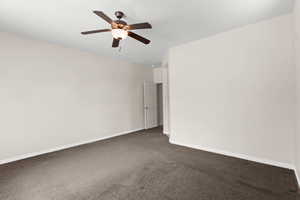 Unfurnished room featuring baseboards, a ceiling fan, and dark colored carpet