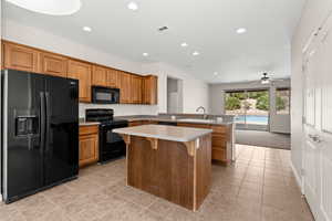Kitchen featuring light tile patterned floors, a peninsula, black appliances, a kitchen island, and a sink