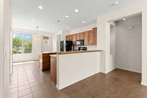 Kitchen with black microwave, fridge with ice dispenser, a peninsula, visible vents, and brown cabinets