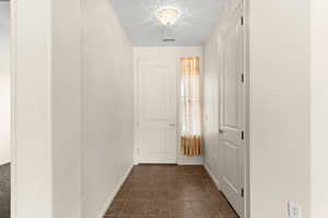 Hall featuring visible vents, baseboards, and dark tile patterned flooring