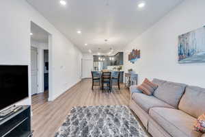 Living room with baseboards, light wood-type flooring, an inviting chandelier, and recessed lighting