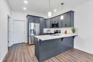 Kitchen featuring a kitchen breakfast bar, a peninsula, light countertops, stainless steel appliances, and a sink
