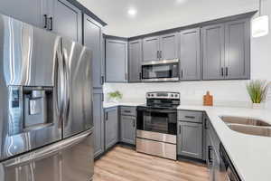 Kitchen featuring gray cabinetry, light wood-style flooring, light countertops, and appliances with stainless steel finishes
