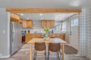 Kitchen with light brown cabinets, light wood-type flooring, beam ceiling, appliances with stainless steel finishes, and a sink