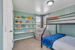 Bedroom with baseboards, carpet, a textured ceiling, and wooden walls